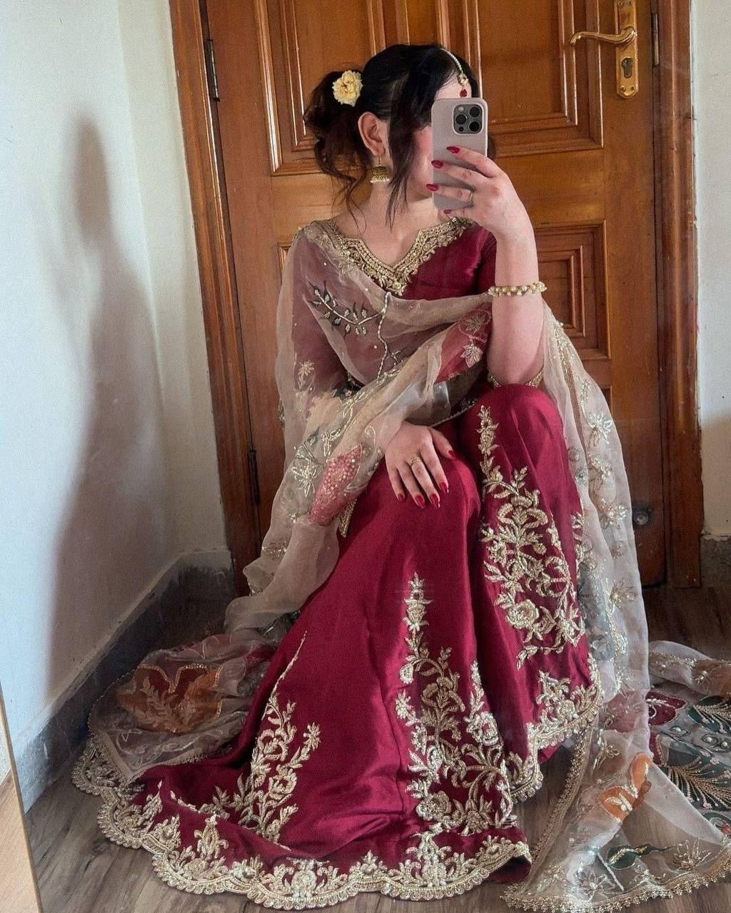 Woman in a maroon saree with gold embroidery sitting in front of a wooden door.