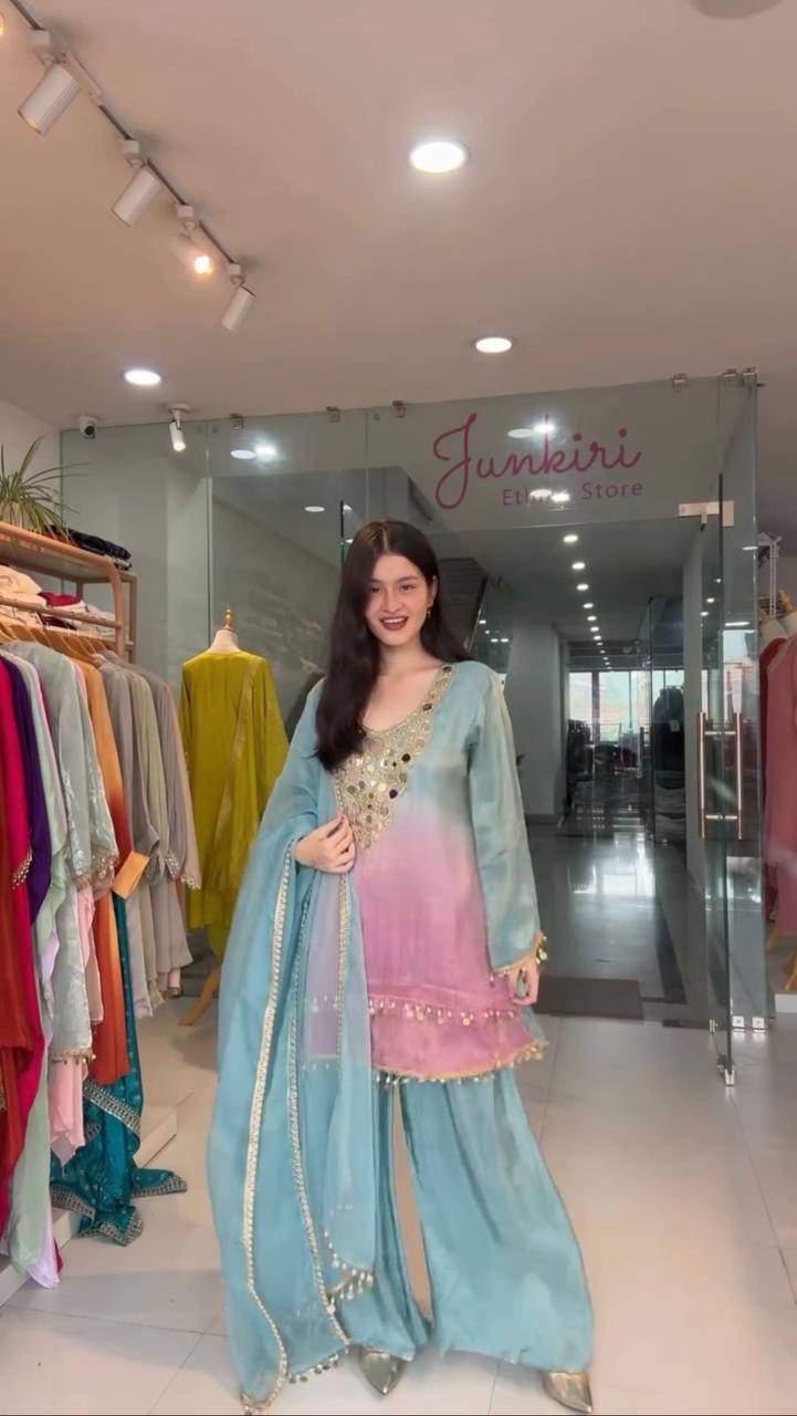 Woman in a light blue and pink traditional outfit standing in a store with 'Junkeri' branding.