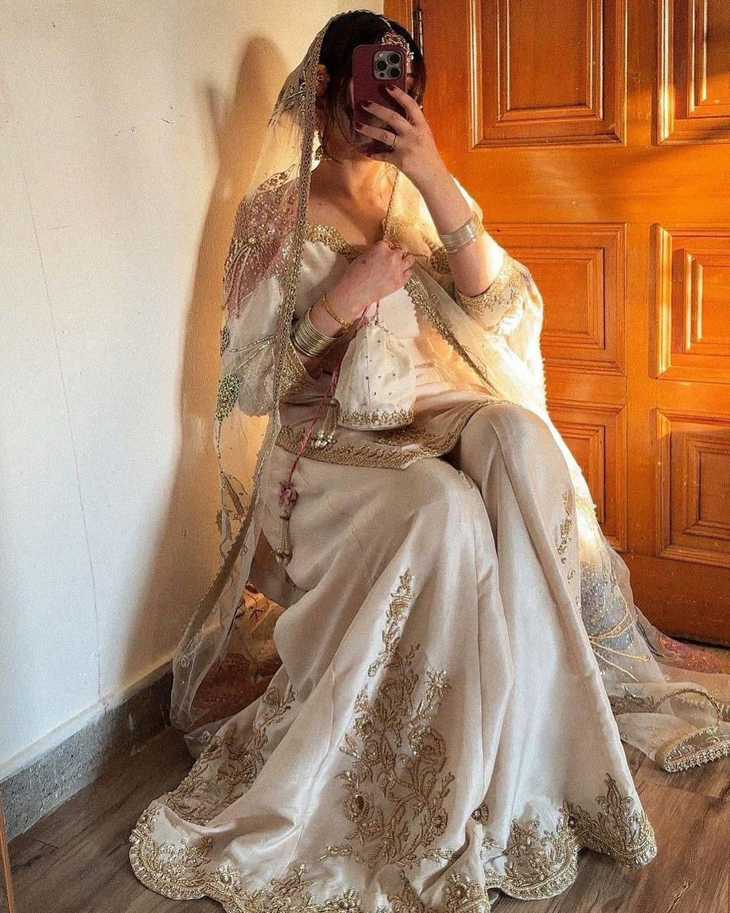 Person wearing a traditional embroidered outfit sitting in front of a wooden door.
