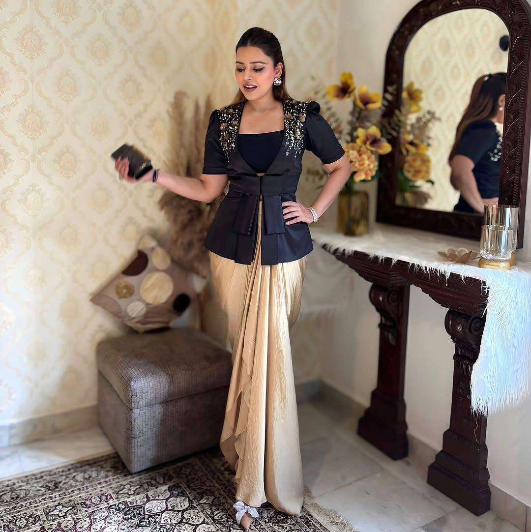 Woman in a black blouse and beige saree standing in a room with decorative elements.